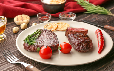 Plate with yummy grilled steaks on wooden table