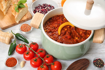 Saucepan with delicious chili con carne on table