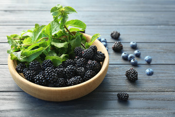 Bowl with fresh mint and ripe blackberries on wooden background