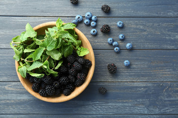 Bowl with fresh mint and ripe blackberries on wooden background