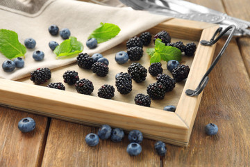 Wooden tray with delicious ripe blackberries and blueberries on table