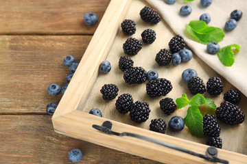 Wooden tray with delicious ripe blackberries and blueberries on table