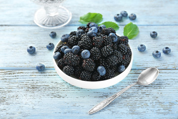 Plate with delicious ripe blackberries and blueberries on wooden background