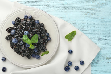 Plate with ripe blackberries and blueberries on wooden background