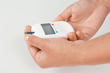 Woman testing glucose level with digital glucometer on white background. Diabetes concept