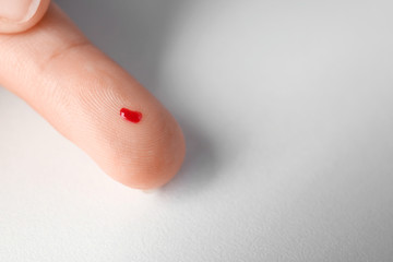 Finger of woman with blood drop for testing glucose level, on white background. Diabetes concept