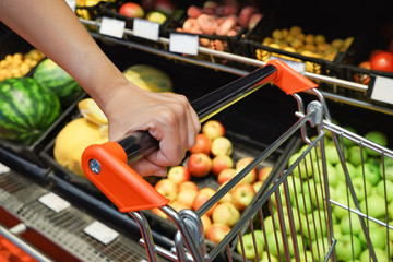 Young woman with cart choosing fruits in supermarket