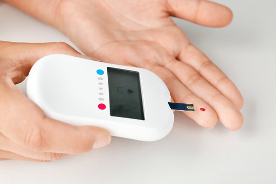 Woman testing glucose level with digital glucometer on white background. Diabetes concept