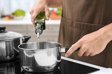 Man pouring cooking oil from bottle into saucepan on stove