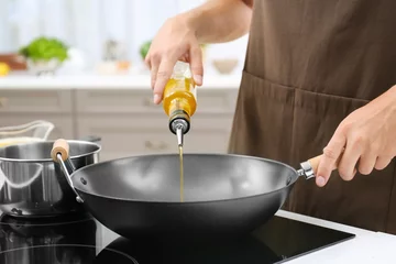 Photo sur Aluminium Cuisinier Man pouring cooking oil from bottle into frying pan on stove