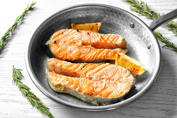 Frying pan with delicious salmon steaks on table