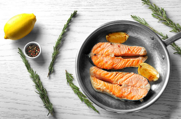 Frying pan with delicious salmon steaks on table