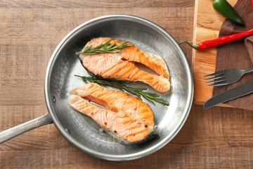 Frying pan with delicious salmon steaks on table