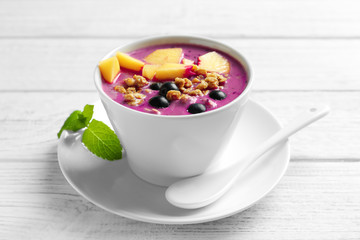 Bowl with acai smoothie, peach and muesli on wooden background