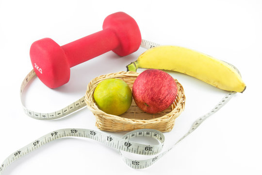 Fitness dumbbells and fruits. Fresh red tasty apple,orange and banana with measuring tape isolated on white