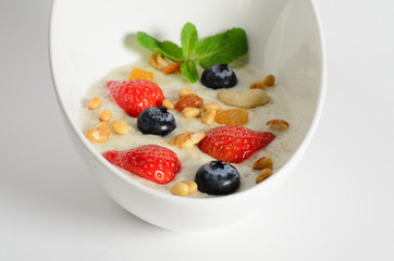 Oat porridge with berries and nuts in a bowl isolated on white background