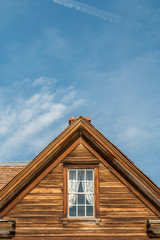 Vintage front of a old wooden building with a window and chimney. The window has a white lace curtain. A blue sky and clouds in the background