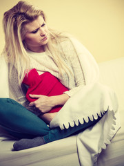 Woman feeling stomach cramps sitting on cofa