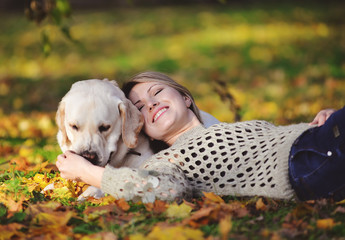 The blonde lies in yellow leaves with her labrador in the park in autumn