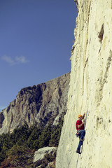 Fototapeta premium Young man climbs on a rocky wall in a valley with mountains.