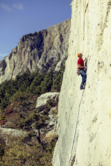 Young man climbs on a rocky wall in a valley with mountains.