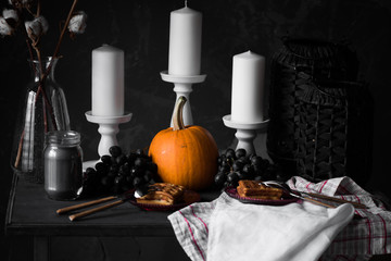 Autumn decor of a table with a pumpkin, white candles, fruits and Viennese wafers