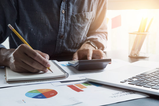 Businessman with calculator and laptop computer counting with cost and writing make notes at office, Business financial concept