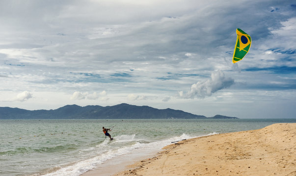 The Brazilian black man rides on the kite. Kite Surfing water sport. Sea with wave and KiteSurf with Flag of Brazil in the air. Stunning cloudy sky Landscape.
