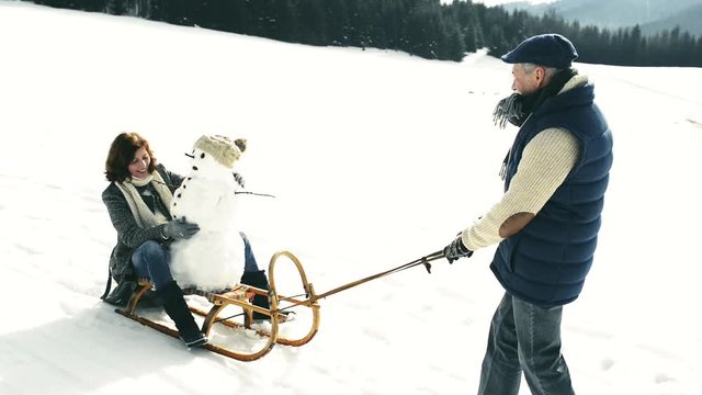 Senior couple pulling a snowman on a sledge in winter nature.