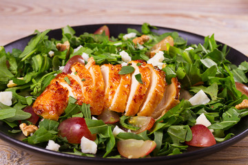 Chicken, grapes and goat cheese salad in black plate on wooden background
