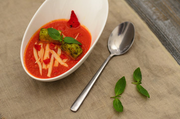 Tomato soup with goat cheese, sun-dried tomatoes and croutons in a bowl with basil and spoon