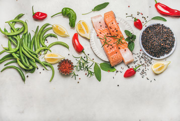 Fototapeta na wymiar Flat-lay of raw salmon fish fillet steaks with vegetables, greens, rice and spices over grey marble background, top view, copy space. Clean eating, alkaline diet, dieting, power boosting concept