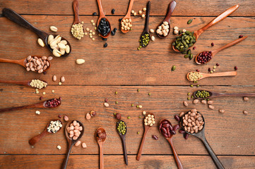 Assortment of beans and lentils in wooden spoon on teak wood background