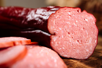 Handmade delicious smoked sausage on burnt wooden cutting board with pile of slices.