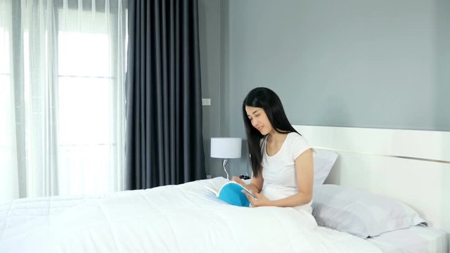 Side view of a Asian beautiful woman sitting in bed and reading a book