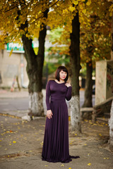 Adult brunette woman at violet gown on autumn fall background.