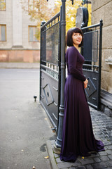Obraz premium Adult brunette woman at violet gown background black iron gates.