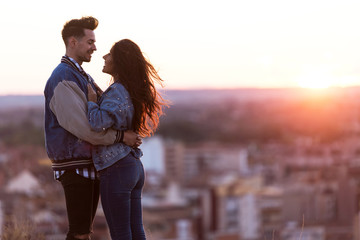 Beautiful young couple in love standing at a building rooftop at the sunset.