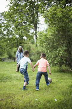 Grandmother looking at twin boys playing soccer in back yard