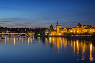 Fototapeta na wymiar Lit Charles Bridge (Karluv most), Old Town and their reflections on the Vltava River in Prague, Czech Republic, at dusk. Copy space.