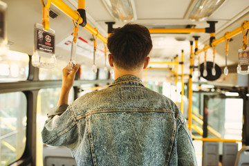 Asian man taking public transport, standing inside bus.