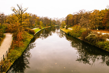 Spree river channel in Berlin during Autumn with fallen leaves on the ground and trees losing their yellow and red leaves in the public park Tiergarten, Berlin, Germany.