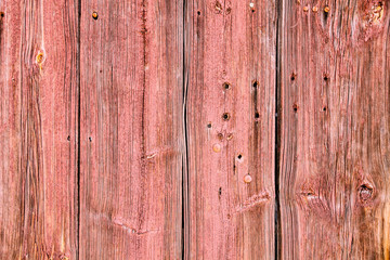 Old grunge and weathered light red wooden wall planks texture with rusted nails and holes due to exposure to the elements outdoors.