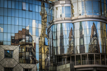 Fototapeta na wymiar Reflection of houses in glass window of modern building. Modern office building exterior, old houses reflected on the glass of a curtain wall.
