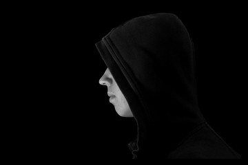 Young teenage bully boy in black hoodie isolated on black background for copy writing. Black and...