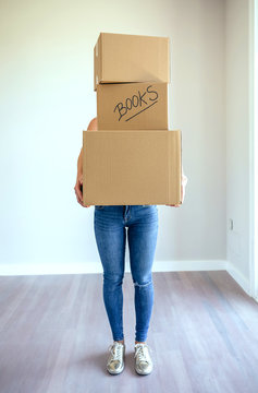 Unrecognizable woman carrying three moving boxes in living room
