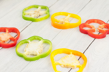 Two row of slices of colored red and green and yellow fresh ripe raw pepper on old rural white wooden planks