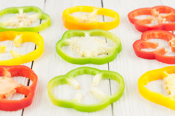 Slices of colored red and green and yellow fresh ripe raw pepper in form square on old rural white wooden planks