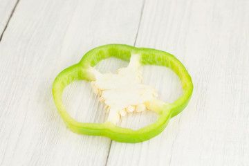 Single slice of green fresh ripe raw pepper on brown cutting board on old rural white wooden planks