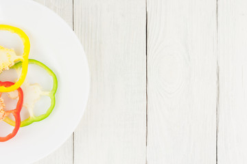 Three slices of colored red and green and yellow fresh ripe raw pepper in ceramic bowl on old rural white wooden planks